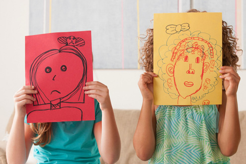 Children holding drawings in front of their faces