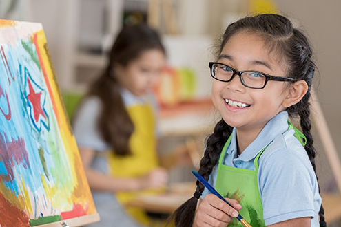 A young girl smiles as she stands in front of a painting she is creating.