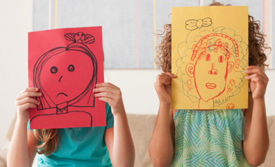 Children holding drawings in front of their faces