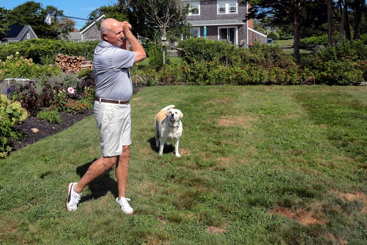 Tom Cioffi practicing his golf swing, accompanied by one of his dogs.