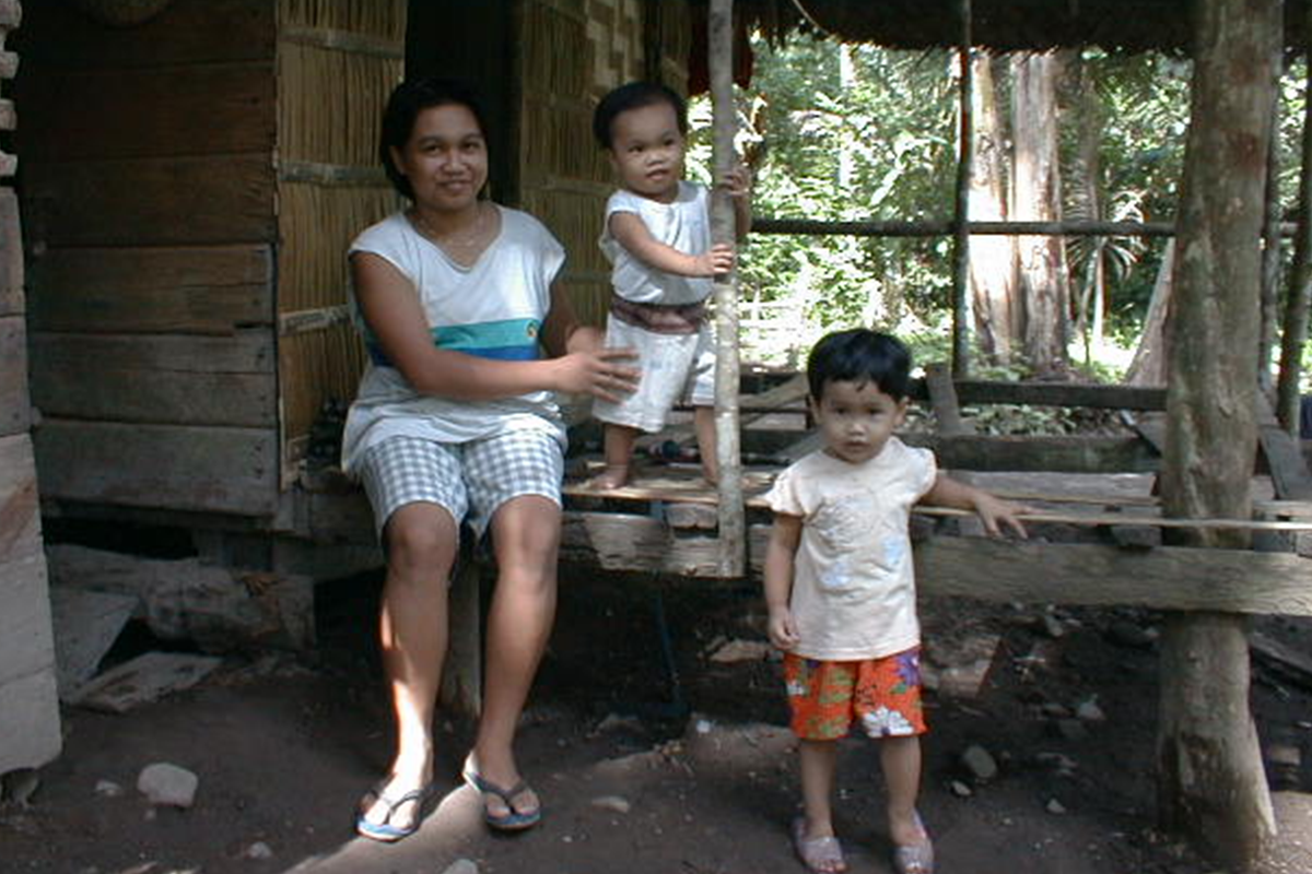 A woman and two children sit outside, under an awning